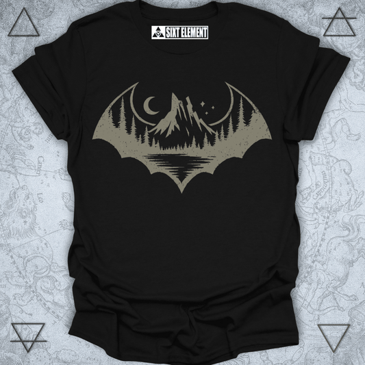 A distressed-style graphic shaped like a bat silhouette, featuring a scenic wilderness landscape inside. The design includes tall pine trees, a mountain range, a crescent moon, stars, and a reflection on a calm lake. The entire image has a rugged, vintage look, perfect for an outdoor or gothic-themed t-shirt.